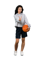 A full-length shot of a Young woman playing basketball smiling and showing victory sign over isolated white background