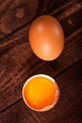 Brown egg and broken egg with yolk on rustic table.