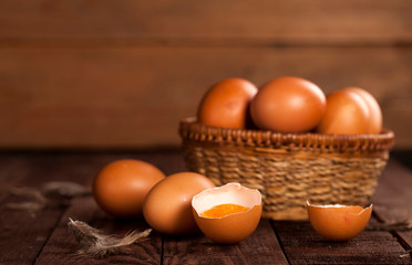 Brown eggs in a basket and broken egg with yolk on rustic table.