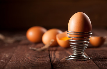 Brown eggs and broken egg with yolk on rustic table.