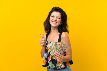 Young woman over isolated yellow background taking a lot of money