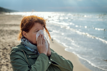 A woman is standing by the sea, using a handkerchief, she has an allergy or severe flu. Concept: Runny nose or protection against infections