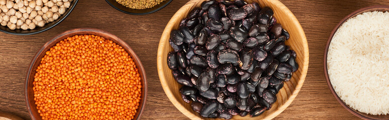 panoramic shot of bowls with red lentil, black beans, white rice and chickpea on wooden surface