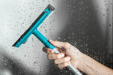 close up cleaning shower glass door with squeegee