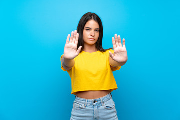 Young girl over isolated blue background making stop gesture and disappointed
