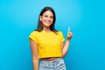 Fototapeta na wymiar Young girl over isolated blue background showing and lifting a finger in sign of the best