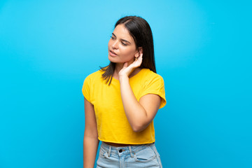 Fototapeta na wymiar Young girl over isolated blue background listening to something by putting hand on the ear