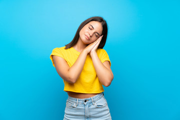 Young girl over isolated blue background making sleep gesture in dorable expression