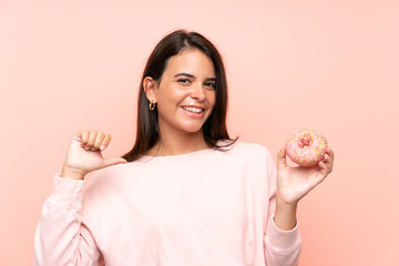 Young girl holding a donut over isolated pink background proud and self-satisfied