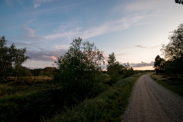 Schotterweg an der Heide im Sonnenuntergang mit grandiosem Himmel