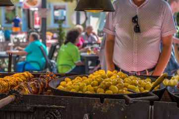 A man stands at a stall where potatoes and grilled shashlik are prepared. Concept: food on vacation