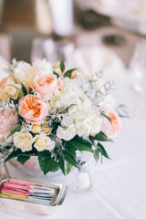 Fine wedding floral arrangement with pink peonies, white roses, dusty miller, and greenery, silver vase, white tablecloth, luxury wedding reception decor