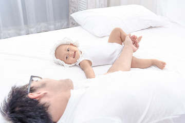 Little baby infant girl laying on white bed smiling to her daddy. Family having a happy time together.
