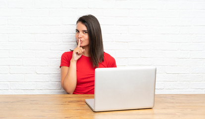 Young girl with pc in a table doing silence gesture