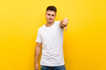 Young handsome man over isolated yellow background showing thumb down with negative expression