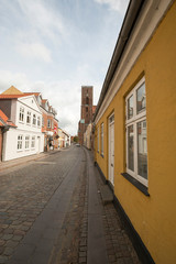 Gelbes Haus in einer Straße die auf einen Kirchturm zuführt