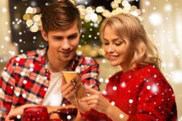 Obraz na płótnie Canvas holidays, technology and celebration concept - happy couple having christmas dinner at home and using smartphone over snow