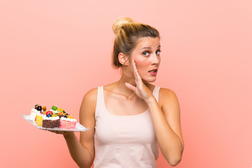 Young blonde woman holding lots of different mini cakes whispering something