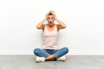 Young blonde woman sitting on the floor with surprise facial expression