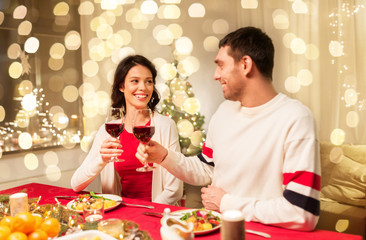 holidays, family and celebration concept - happy couple having christmas dinner at home and drinking red wine and clinking glasses