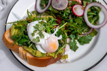 Healthy Breakfast Avocado Sandwich with Fried Egg on wholemeal Bread Toast served with mixed season fresh salad, on a plate outside of cafe or hotel restaurant. 