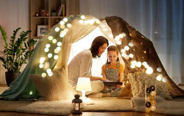 family, hygge and technology concept - happy mother and little daughter with tablet pc computer in...