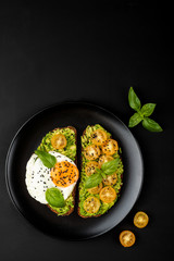 Open sandwiches with avocado guacamole, yellow cherry tomatoes, fried egg and basil on a black plate on the black background. Top view. Copy space.