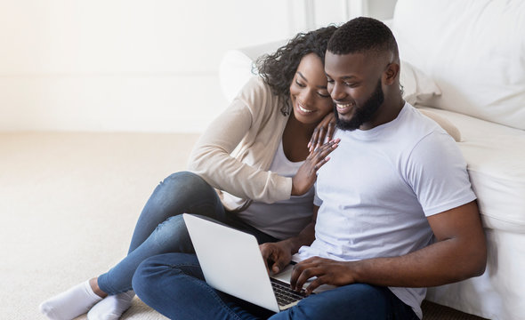 African couple web surfing on laptop while sitting at home