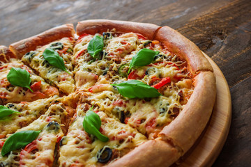 tasty sliced pizza with basil leaves on cutting board on wooden table