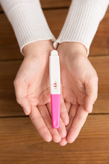 fertility and maternity concept - woman hands holding positive pregnancy test with two stripes over wooden boards background