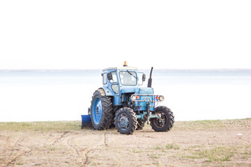 Obraz premium Tractor working on the farm, a modern agricultural transport, cultivation of fertile land, tractor on cloudy sky background, agricultural machine