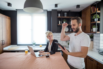 Fototapeta premium Couple in kitchen in the morning. Happy excited man cheering satisfied with results on laptop.