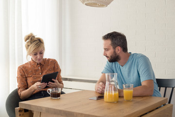 Couple sitting by the table. They are discussing something on tablet.