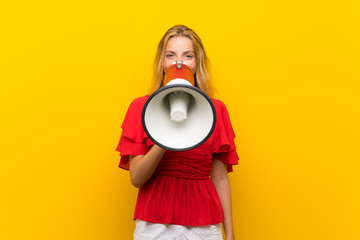 Blonde young woman over isolated yellow background shouting through a megaphone