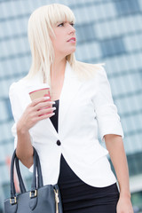 young blonde business woman in white blazer drinks coffee