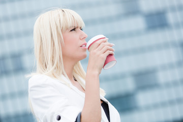 young blonde business woman in white blazer drinks coffee