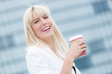 young blonde business woman in white blazer drinks coffee