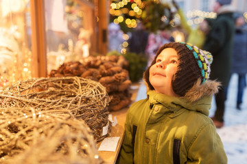 holidays, childhood and people concept - happy little boy at christmas market in winter evening