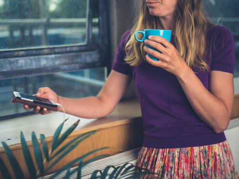 Woman drinking coffee and charging her phone by window