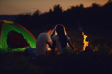 Romantic camping. A young couple sitting by the bonfire