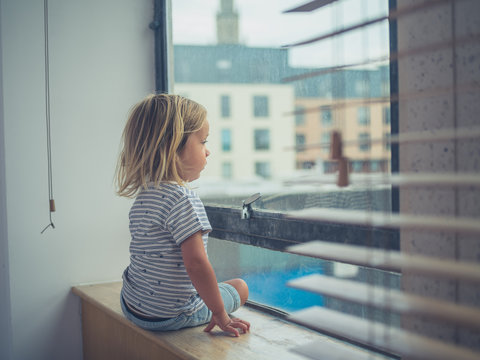 Little toddler sitting by the window of city apartment