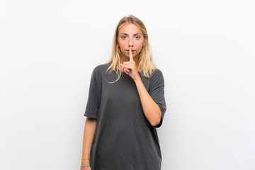 Blonde young woman over isolated white background showing a sign of silence gesture putting finger...
