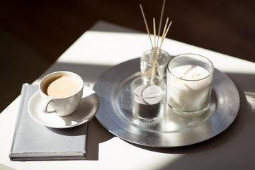 hygge and aromatherapy concept - coffee, candles, book and aroma reed diffuser on table