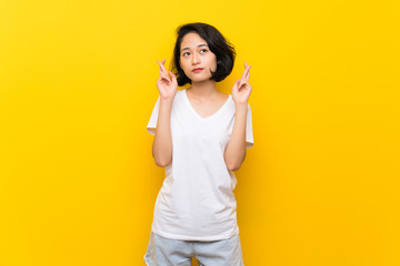 Asian young woman over isolated yellow wall with fingers crossing and wishing the best