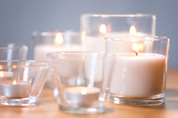 decoration, hygge and cosiness concept - burning white fragrance candles on wooden table