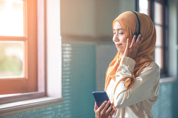Portrait of a smiling young modern arabian woman closing eyes, holding mobile phone and listening the music to headphone.
