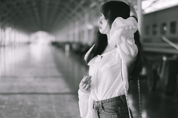 Fototapeta premium Asian young woman standing alone in a train station waiting for something with boredom and moody, street backgrounds and natural light, vintage style.