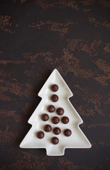 Christmas tree-shaped plate with cherry-filled chocolates on a dark brown background. Top view. Vertical.