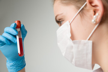 young woman with medical gloves and medical face mask holding a blood probe