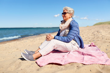 people and leisure concept - happy senior woman in sunglasses and jacket on beach in estonia